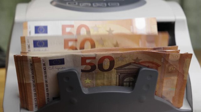 Slow motion close up shot of an automatic banknote counter machine fast processing a stack of fifty euro paper bills. Cinematic financial concept of cash flow, banking operations, currency details