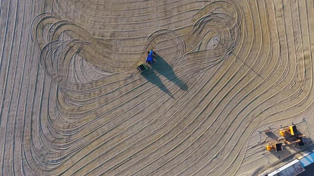 Top-down aerial view of a beach cleaning tractor raking sand on Ryde Beach, creating circular patterns while preparing the shoreline for visitors.