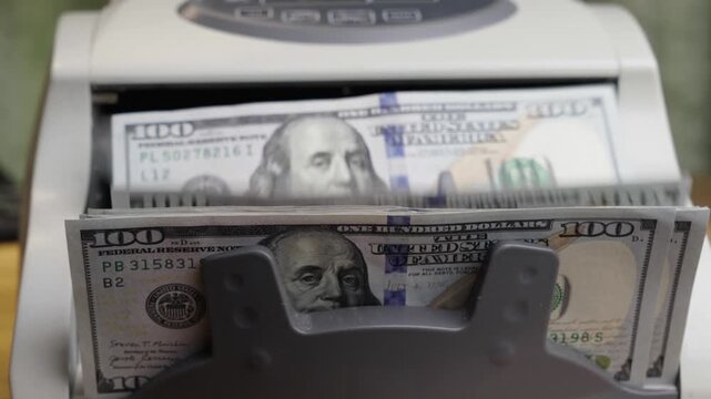 Slow motion close up shot of an automatic banknote counter machine processing a stack of one hundred American dollar bills. Cinematic financial concept of global business, cash flow, wealth