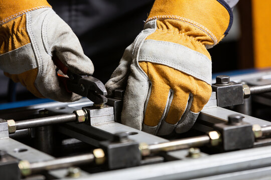 Close-up of hands wearing work gloves tightening a bolt with pliers on machinery