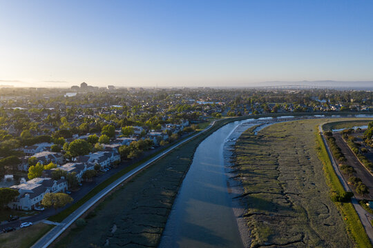 Redwood Shores waterfront homes along a tidal slough at sunset, showing suburban development integrating with marshland habitat and sustainable bay-area green space ecology