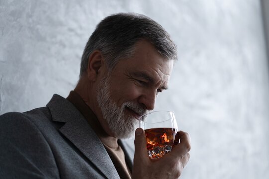 Confident mature businessman chilling relaxing drinking enjoying whiskey against grey wall.