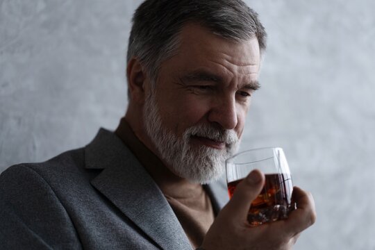 Confident mature businessman chilling relaxing drinking enjoying whiskey against grey wall.