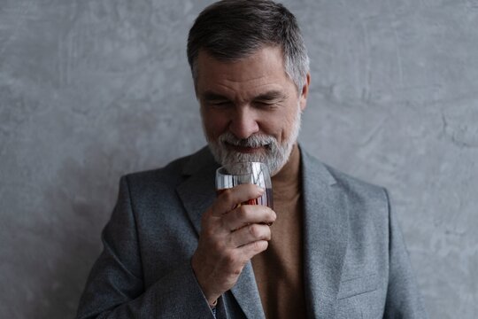 Confident mature businessman chilling relaxing drinking enjoying whiskey against grey wall.