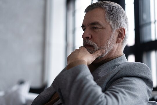 Portrait of handsome bearded mature businessman looking away thoughtfully while sitting on sofa.