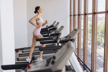 Fototapeta premium Young woman running on treadmill in a modern fitness gym, engaging in cardio workout for health and wellness