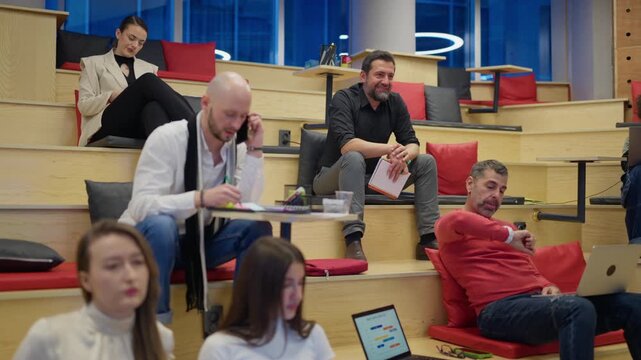 A diverse group of professionals are focused on their tasks in a contemporary tiered office. Coworkers are engaged in discussion and using technology in a collaborative workspace