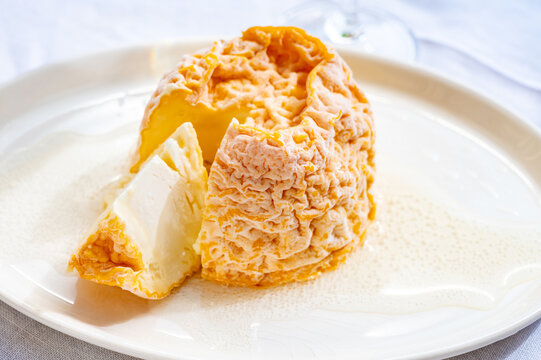 Small, round Langres cheese with orange washed rind and creamy center on a board, spooned and paired with Champagne
