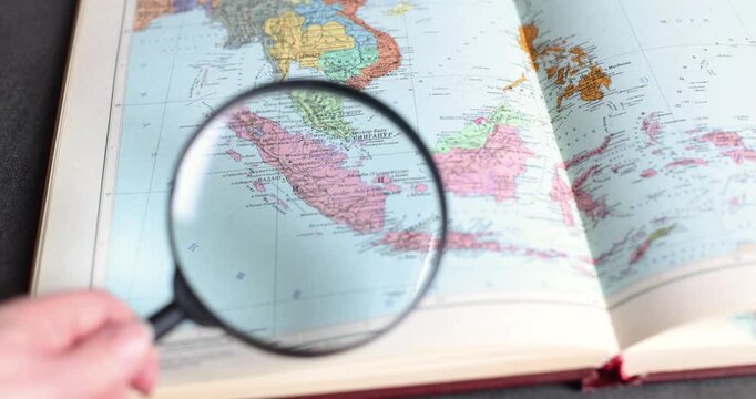 Close-up of a hand holding a magnifying glass over a world map