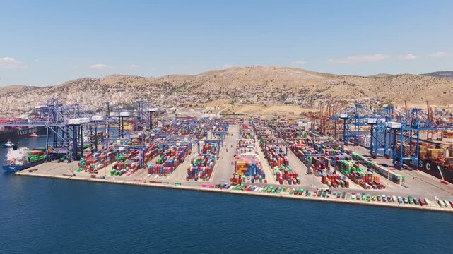 Aerial perspective of a bustling commercial port with colorful shipping containers stacked in the terminal, while large gantry cranes load and unload cargo ships docked at the quay