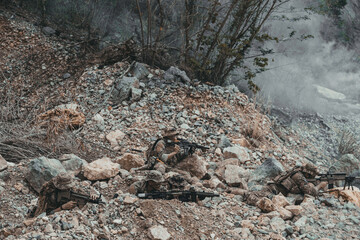 Obraz premium A squad of armed military soldiers taking cover on a rocky hillside during an intense combat mission. Tactical team holding defensive positions with smoke in the background in a warfare concept.