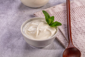 Creamy plain yogurt in white bowl with fresh mint garnish on stone table © Andrei Starostin