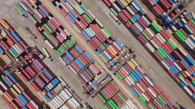 Colorful shipping containers stacked in a large commercial port with gantry cranes moving cargo, representing global trade, logistics, and the supply chain industry from an aerial perspective