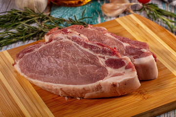 Fototapeta premium Raw pork loin chops on bamboo cutting board with rosemary, garlic, and tomatoes