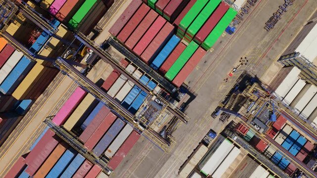 Impressive top-down aerial perspective showing gantry cranes moving and stacking colorful shipping containers in a busy industrial port terminal, showcasing the global logistics and trade industry