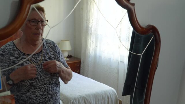 An older woman tries on a gold choker while looking in the mirror..