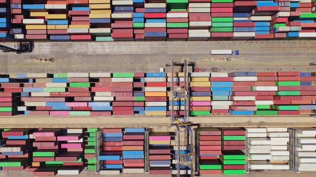 Top-down aerial perspective showing stacks of colorful shipping containers, gantry cranes, and cargo ships in a busy commercial harbor, illustrating the concept of global trade and logistics