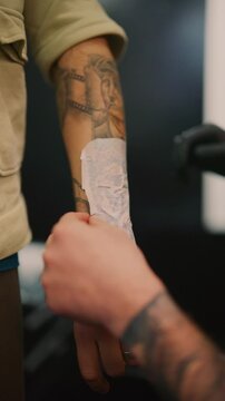 A tattoo artist carefully applies a new stencil design onto a client's arm. The process of transferring a tattoo pattern onto skin is shown in close-up