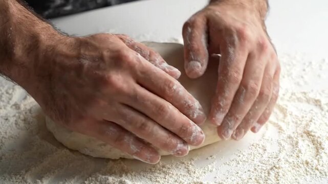 Closeup of a person kneading fresh dough on a floured surface in a kitchen