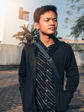 Young Man in Layered Black Outfit with Patterned Shirt Posing Outdoors in Morning Light