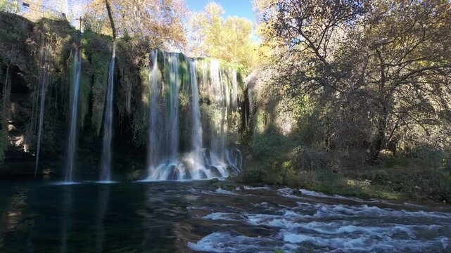 Scenic duden waterfall with multiple streams splashing over mossy rocks into river amid autumn forest antalya.