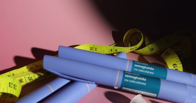 Camera moving in on medical semaglutide glp1 injector devices near replacement needles and a yellow tape measure on pink gradient.