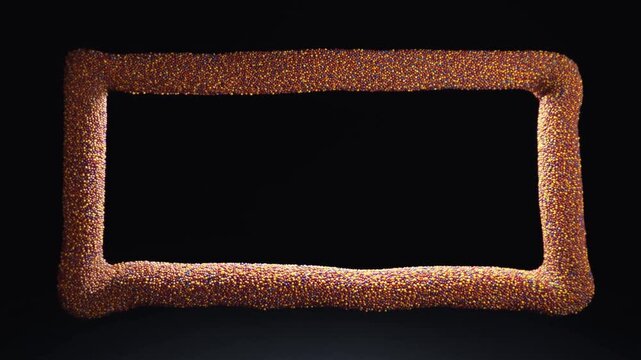 Slow pan of rectangular candy sprinkle frame rotating slightly on black studio backdrop close up tabletop shot