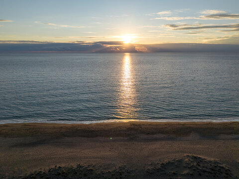 Drone view of a sandy Elea beach in Greece at sunset with calm sea and sun reflection