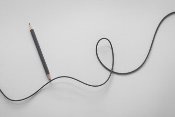 Obraz premium A pencil lies next to a long, curved black cord on a plain surface.