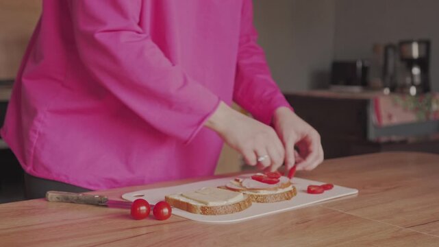 A woman stuffs a sandwich with sausage and tomatoes. Cooking at home.
