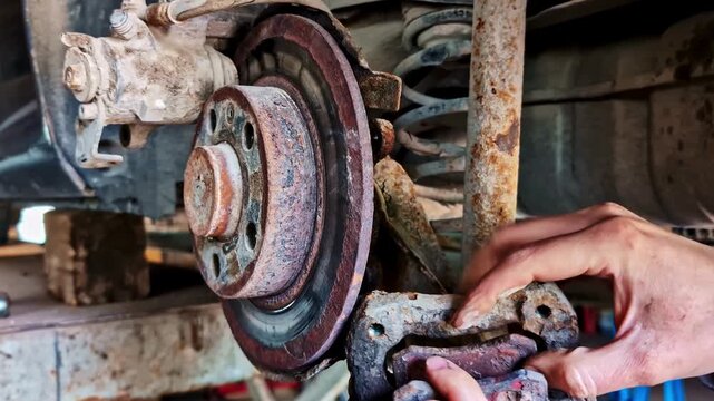 Mechanic removing rare brake caliper from rusted brake disk during repair in workshop.