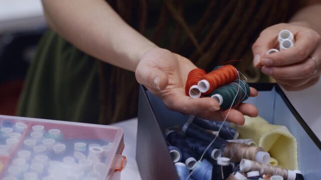 Woman's hands picking a spool of red thread from a box with a colorful assortment for sewing