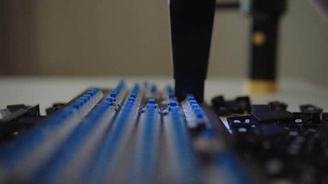 Detailed close-up view of small vacuum cleaner removing dust, hair, debris from blue switches of disassembled mechanical gaming keyboard during routine electronic maintenance. Shooting in slow motion