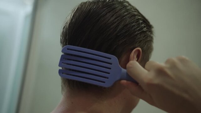 Closeup of man head from behind as he combs wet hair back, focusing on morning routine, personal grooming, hairstyling before starting day in bathroom. Shooting in slow motion