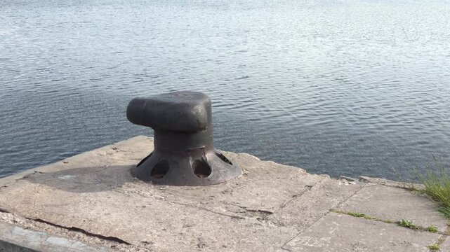 Old mooring bollard on a stone pier by the river, calm water surface as background