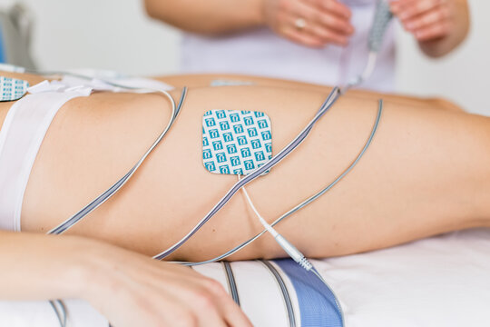 Electrostimulation body treatment procedure with electrode pads on female thigh close up.