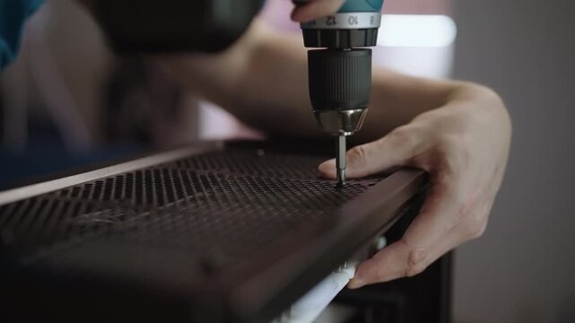 Close-up view of skilled technician using electric screwdriver to assemble personal computer, screwing top panel grill into case during custom pc build, repair service. Shooting in slow motion