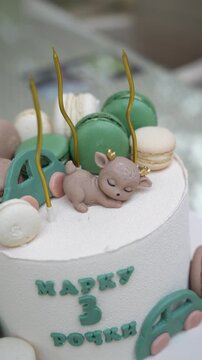 A custom decorated white birthday cake with green macarons and candles for a three year anniversary celebration, birthday cake decoration, third birthday party, custom sweet dessert.