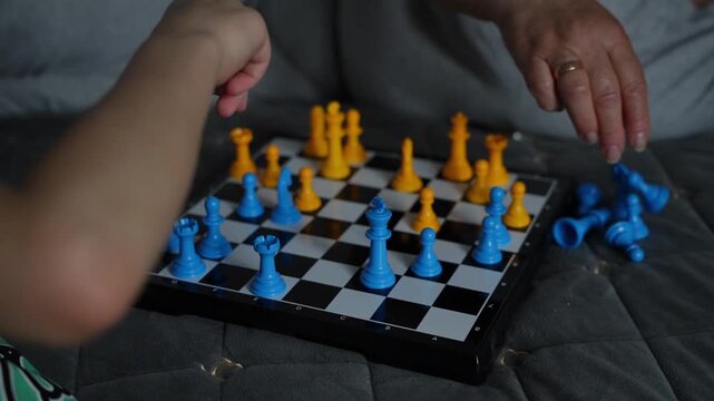 Close up of children playing chess on a board with yellow and blue plastic pieces on a bed, kids playing chess, logical board game, indoor leisure activity.