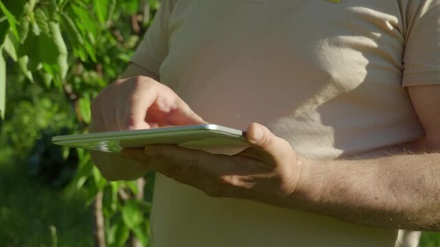 Agronomist using a tablet outdoors, with his fingers tapping the screen while surrounded by lush greenery, highlighting the integration of technology within a natural environment