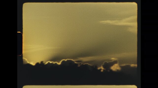 Slow camera pan moving across glowing golden sunset clouds above a dark silhouette of trees on the horizon captured on retro super 8 film