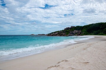 Obraz premium Pristine white sand beach with turquoise waves and rocky shoreline - Seychelles