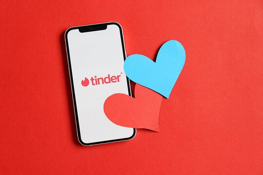 Salvador, Brazil - June 2, 2026: Tinder mobile app displayed on a smartphone screen next to paper hearts on a red background. Online dating and modern romance. Tinder app. 