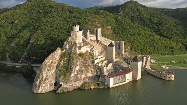 Aerial around view of Golubac medieval fortress on cliff above Danube river at sunset, historic landmark in Serbia, 4k