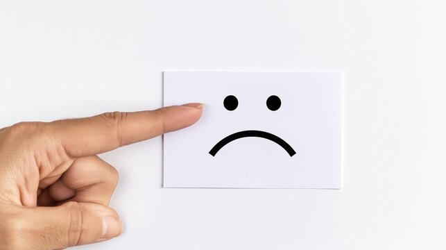Hand indicating a sad face drawing on a white paper card, representing negative customer experience, poor service review, and low rating for evaluation
