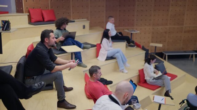 A diverse group of professionals attends a business presentation in a modern, collaborative workspace. Engaged colleagues listen while one employee presents on a large screen