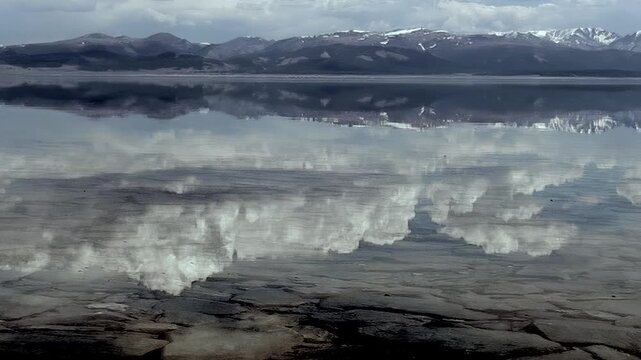 Witness the stunning reflections on Lake Hovsgol, Mongolia, where clouds and distant snow-dusted peaks paint a sublime picture.
