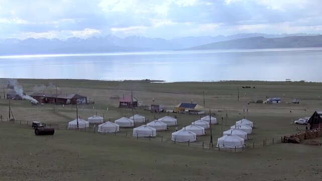 Witness daily life unfolding at traditional ger camp by Lake Khuvsgul in Mongolia. White yurts cluster near permanent structures, smoke billowing softly as residents begin their day, embraced nature.