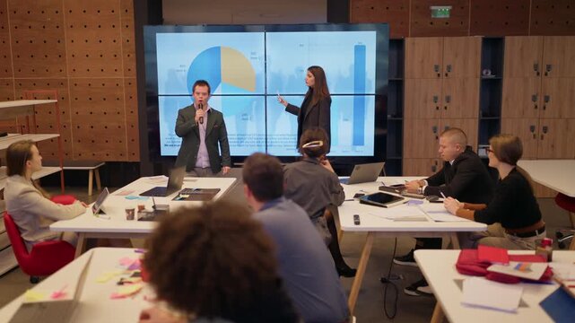 Businesspeople engage in a dynamic presentation, analyzing data and project timelines on a large screen. Employees gather in a modern office setting for a collaborative meeting and training session