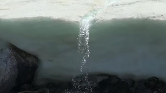 Narrow column of crystal-clear water gushes from melting expanse of ice at Lake Khuvsgul, Mongolia. Lively current plunges onto dark rocks below, signaling vibrant arrival of spring's thaw.